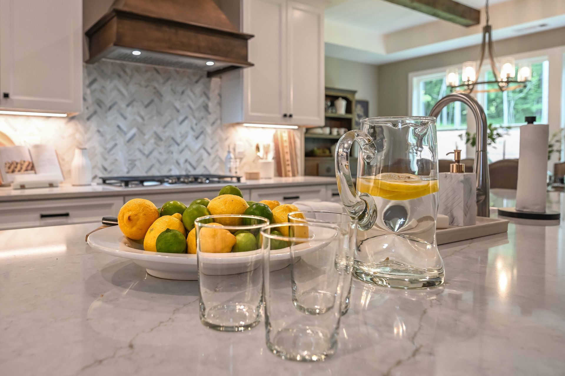 A kitchen counter with a pitcher of water and a plate of lemons and limes.