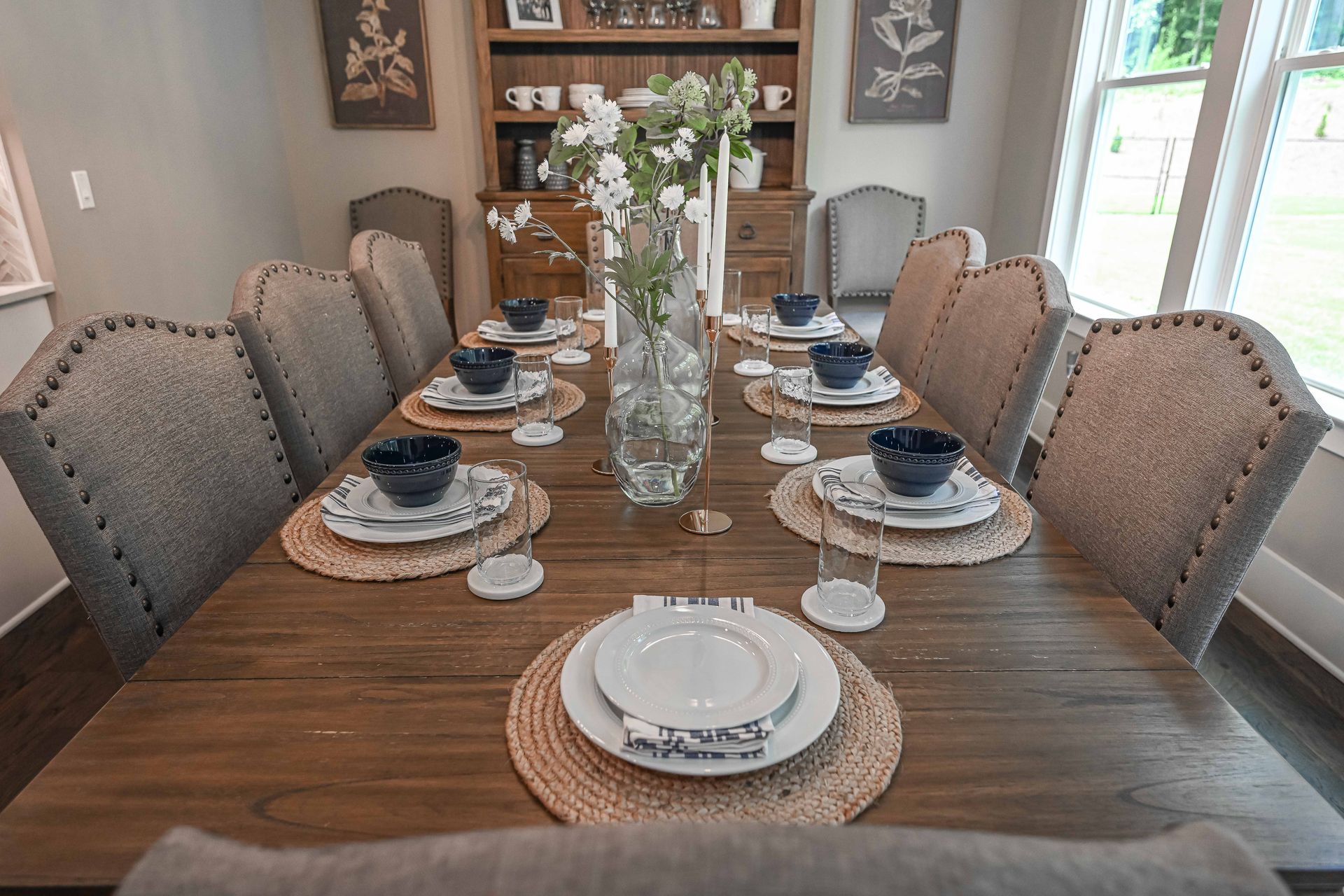 A dining room table with plates , bowls , and a vase of flowers on it.