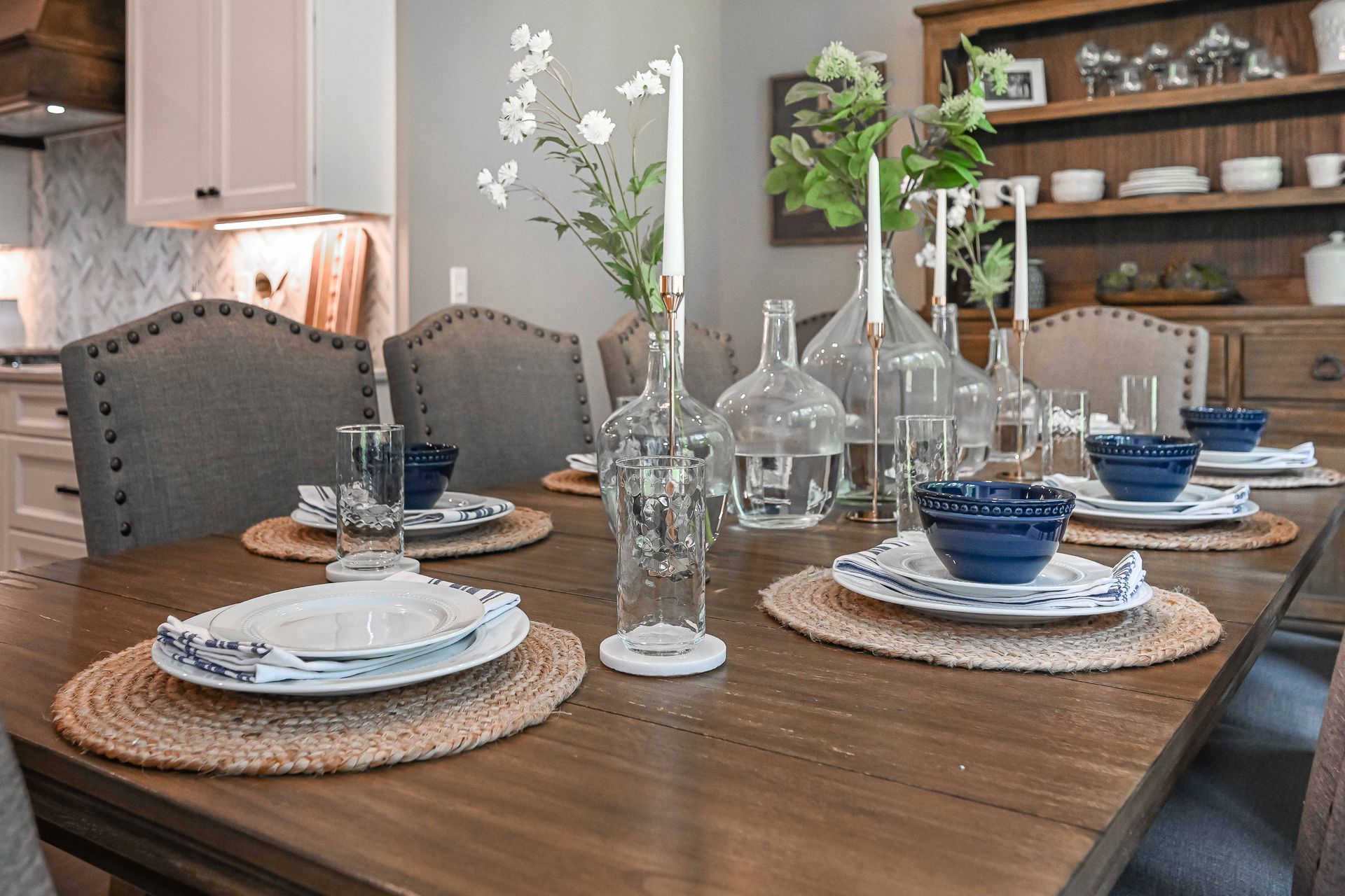 A dining room table with plates , bowls , candles and vases on it.
