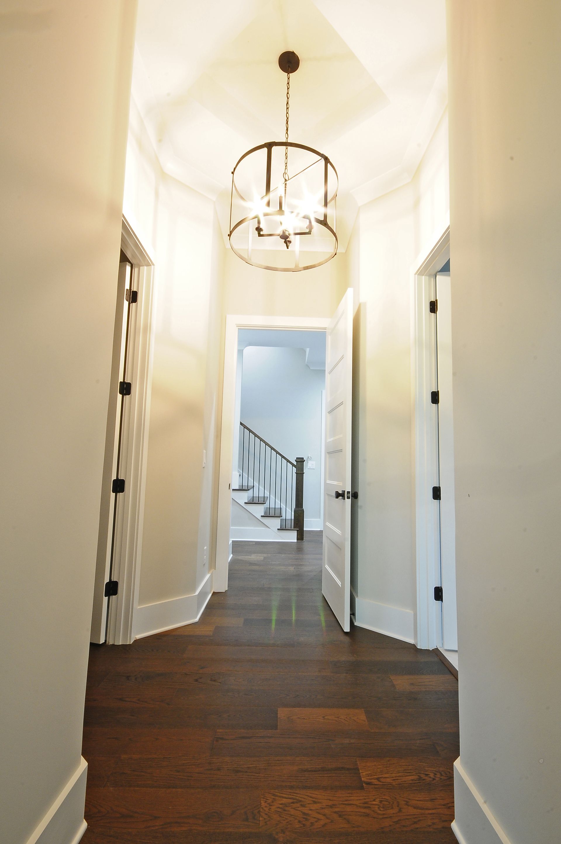 A hallway with wooden floors and a chandelier hanging from the ceiling.