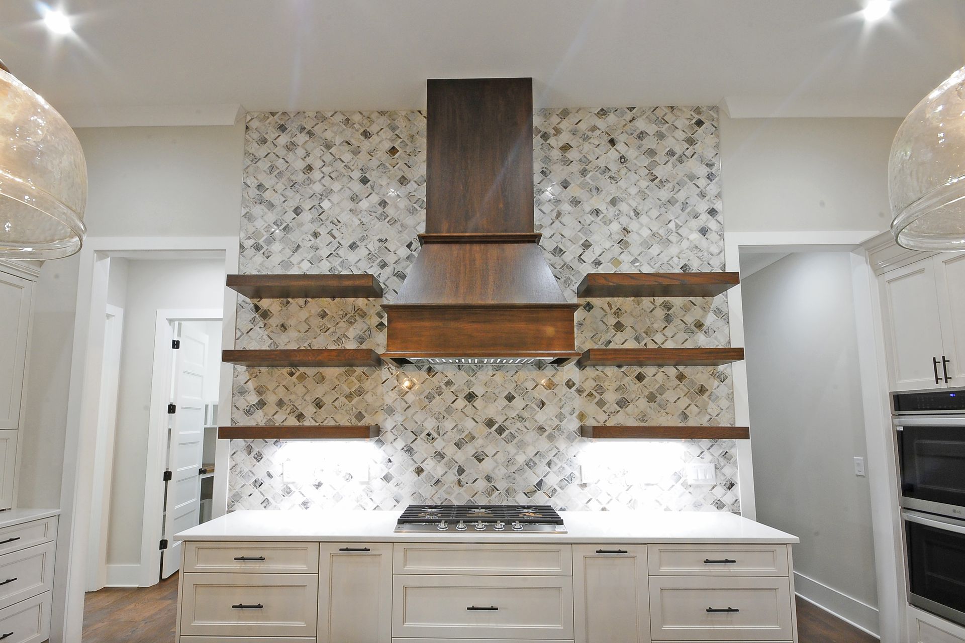 A kitchen with white cabinets , a stove , a hood and shelves.