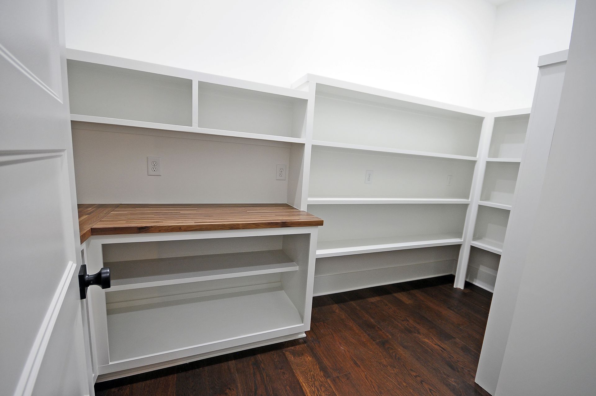 An empty pantry with white shelves and a wooden counter top.