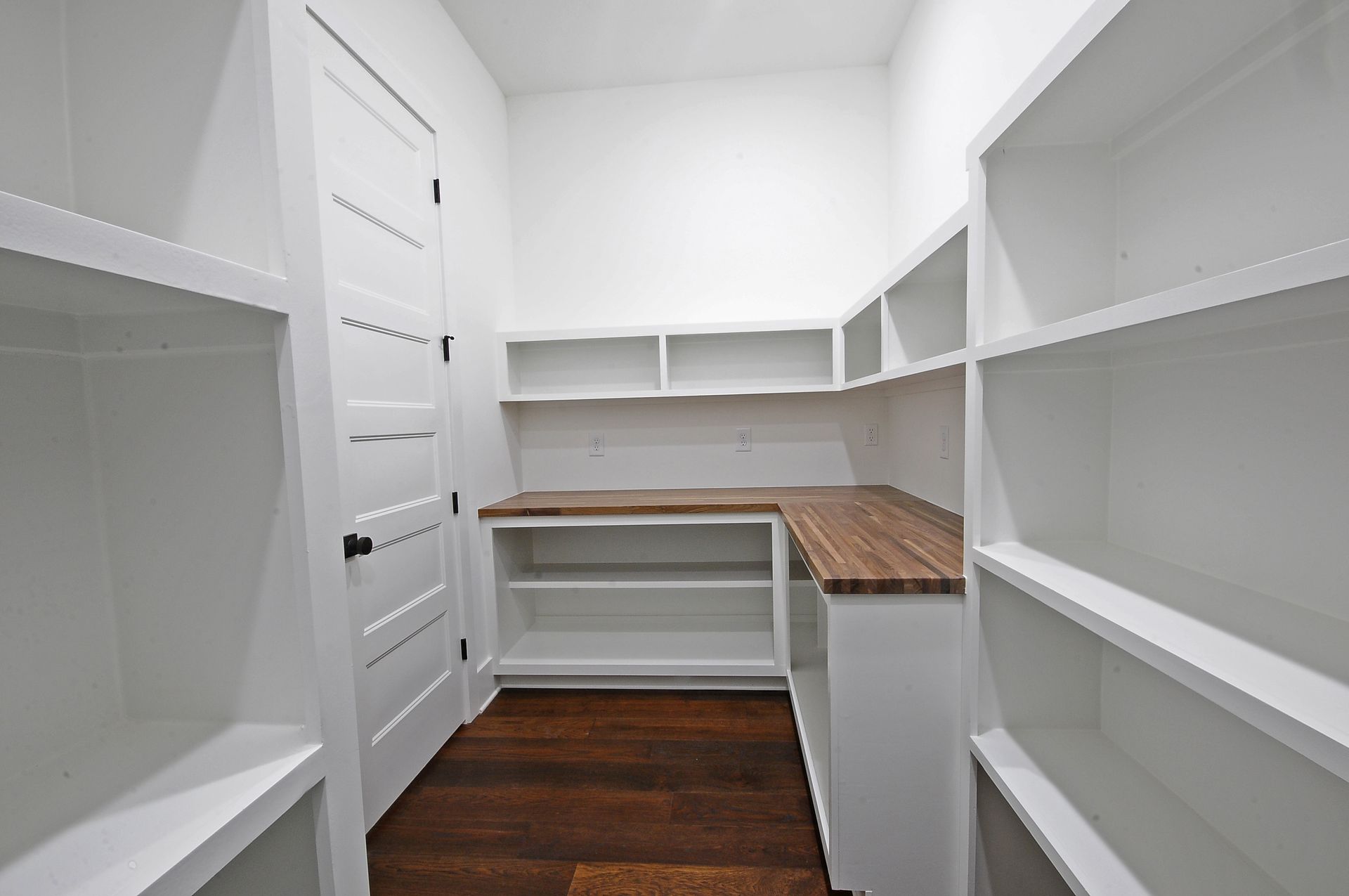 A pantry with white shelves and a wooden counter top.