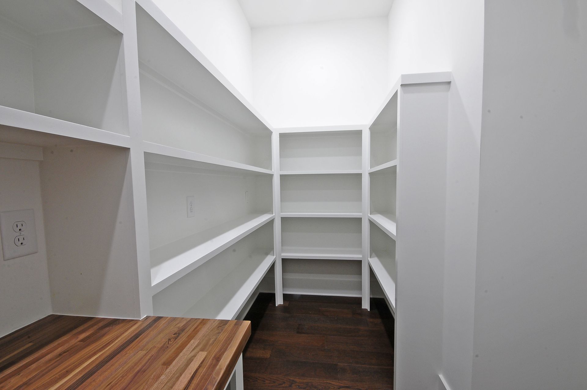 A pantry with white shelves and a wooden counter top.