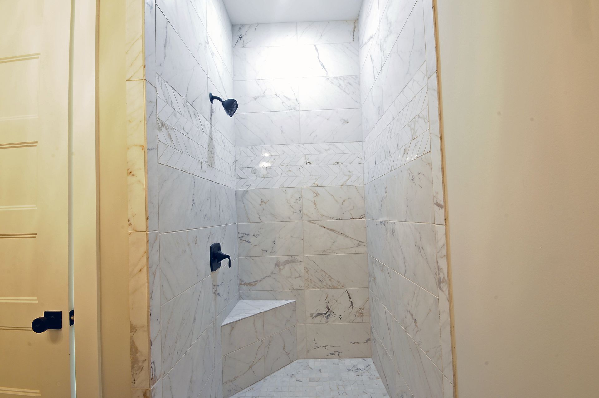 A bathroom with a walk in shower with marble tiles and a bench.