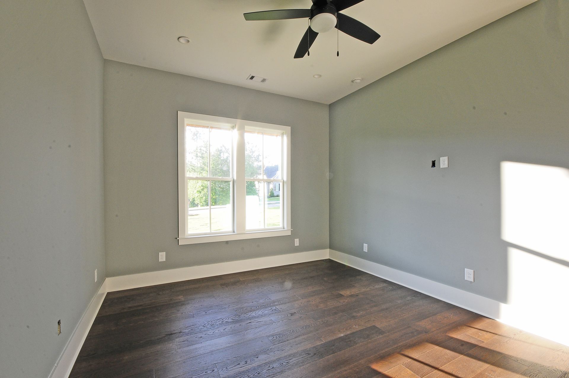 An empty room with a ceiling fan and two windows.