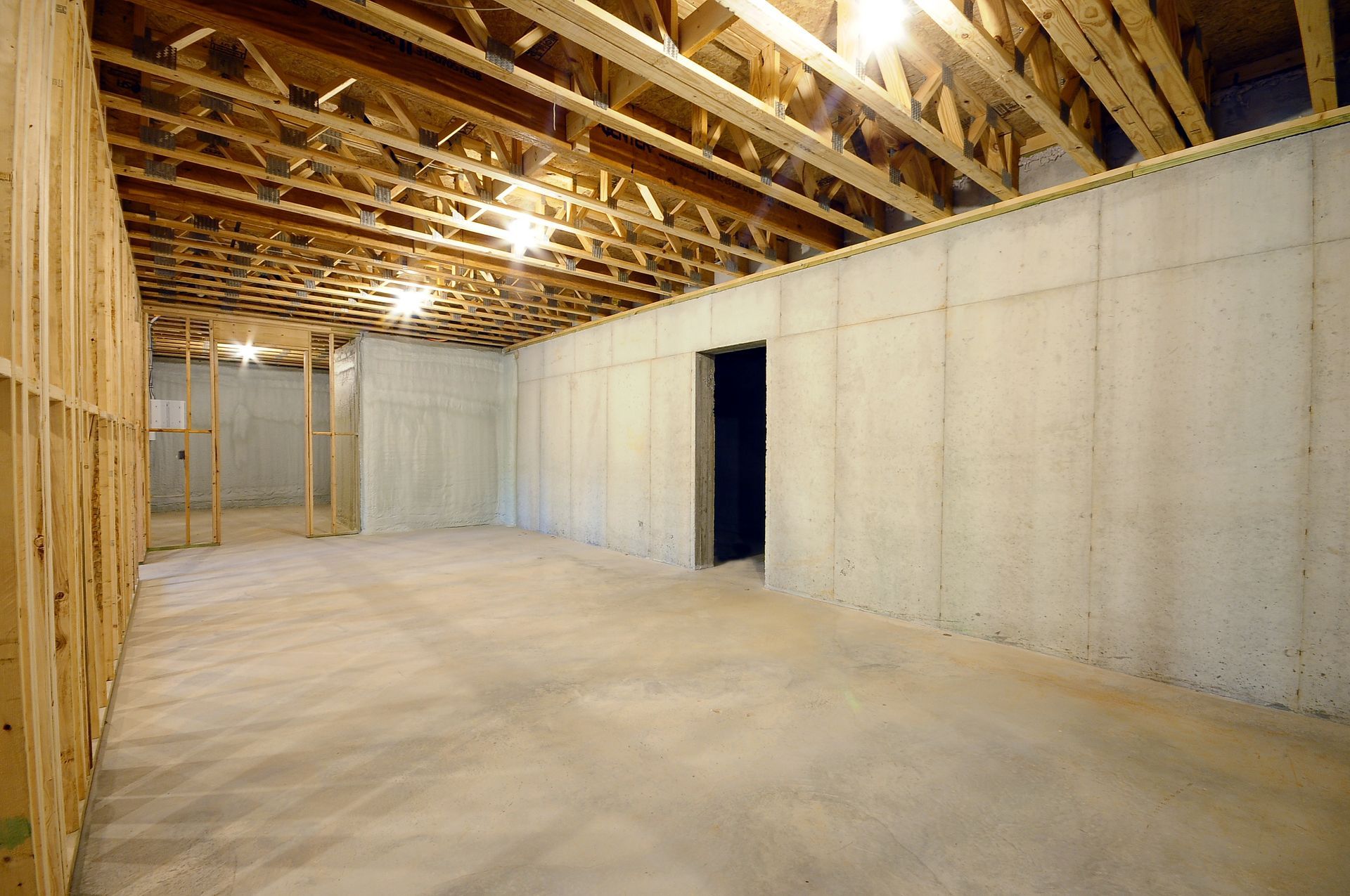 An empty basement with concrete walls and a wooden ceiling.