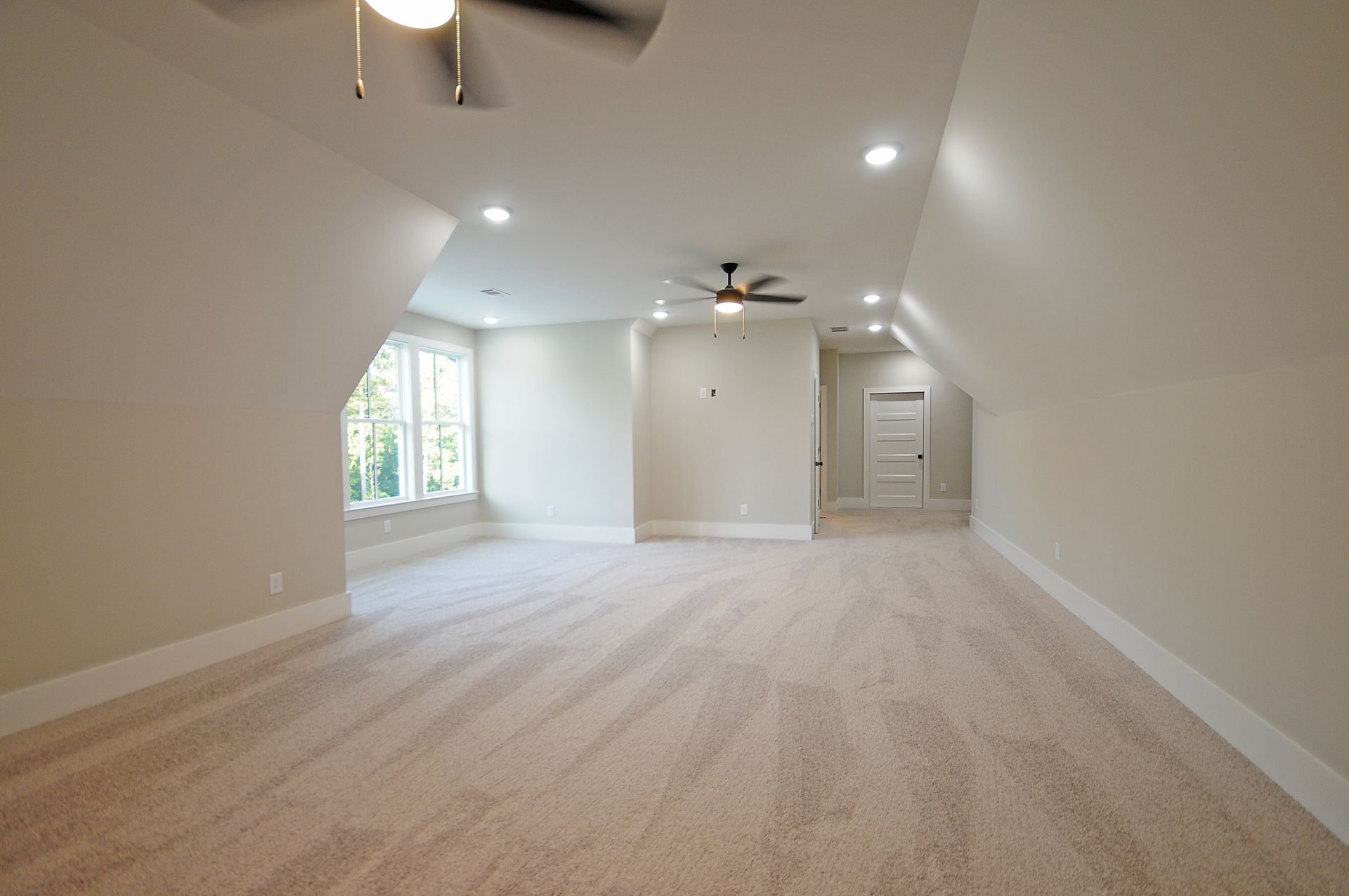 An empty room with a ceiling fan and a large window.