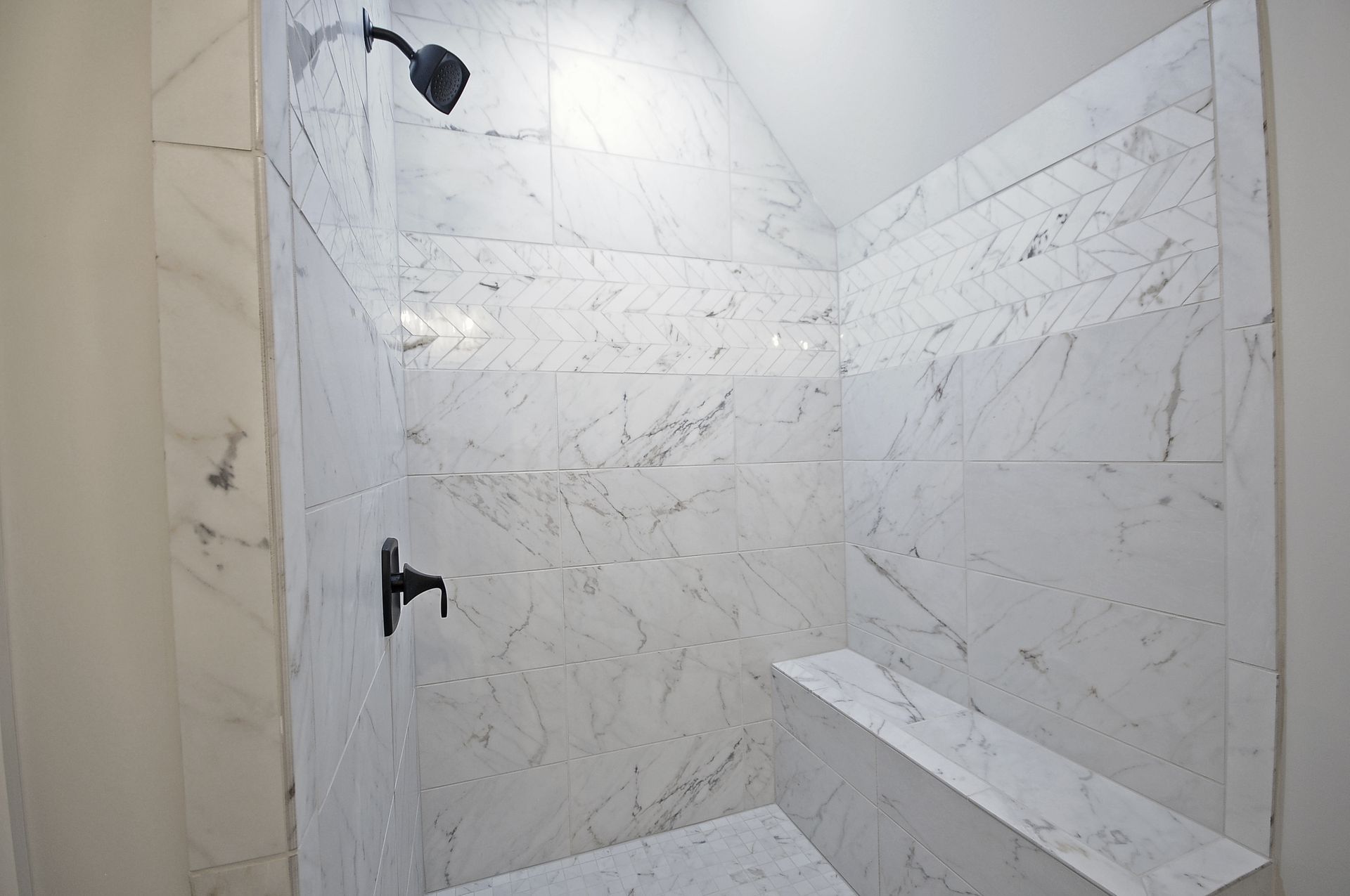 A shower with marble tiles and a black shower head.