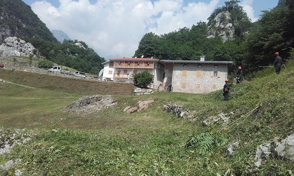 Delle case in montagna viste da lontano e dei giardinieri al lavoro