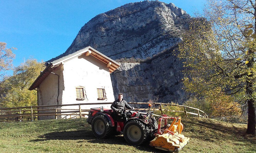 Un uomo su un mezzo agricolo è accanto una casa e una montagna
