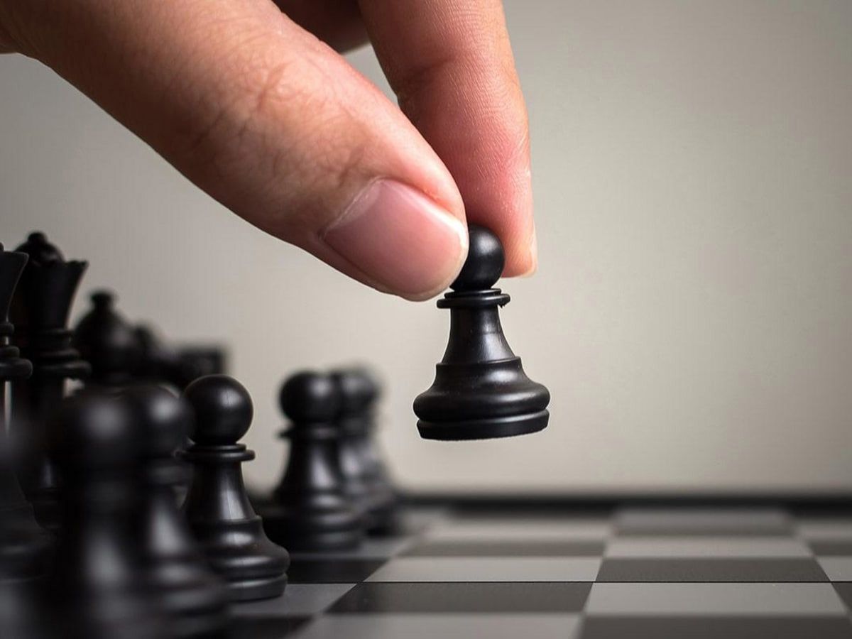 Una mano sostiene un peón negro en un tablero de ajedrez.