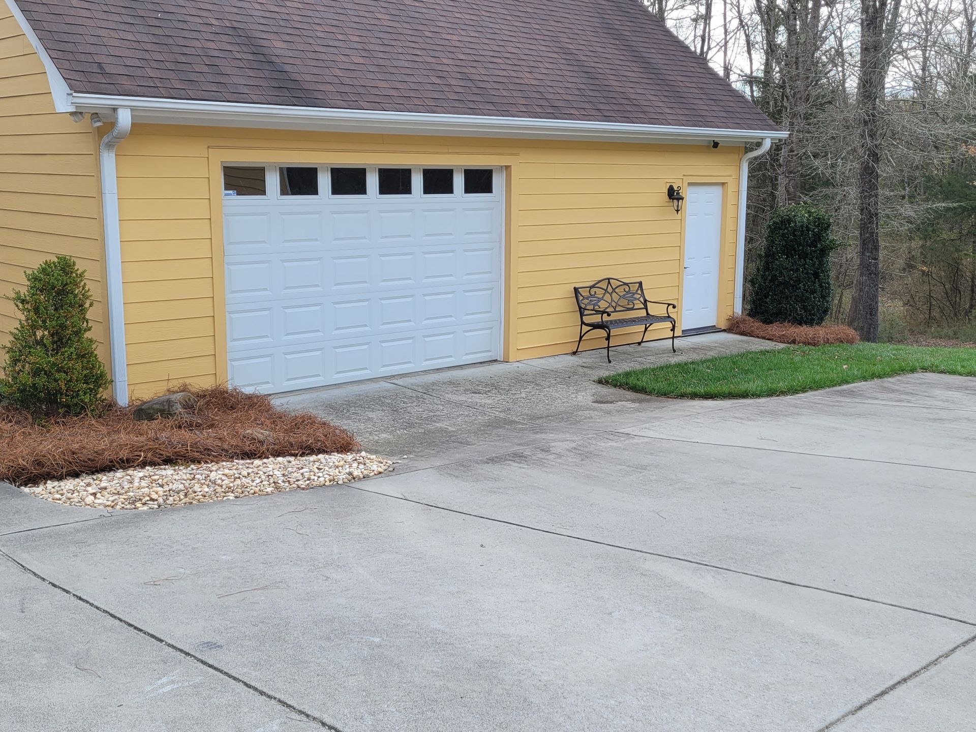 A yellow garage with a white garage door and a bench in front of it.