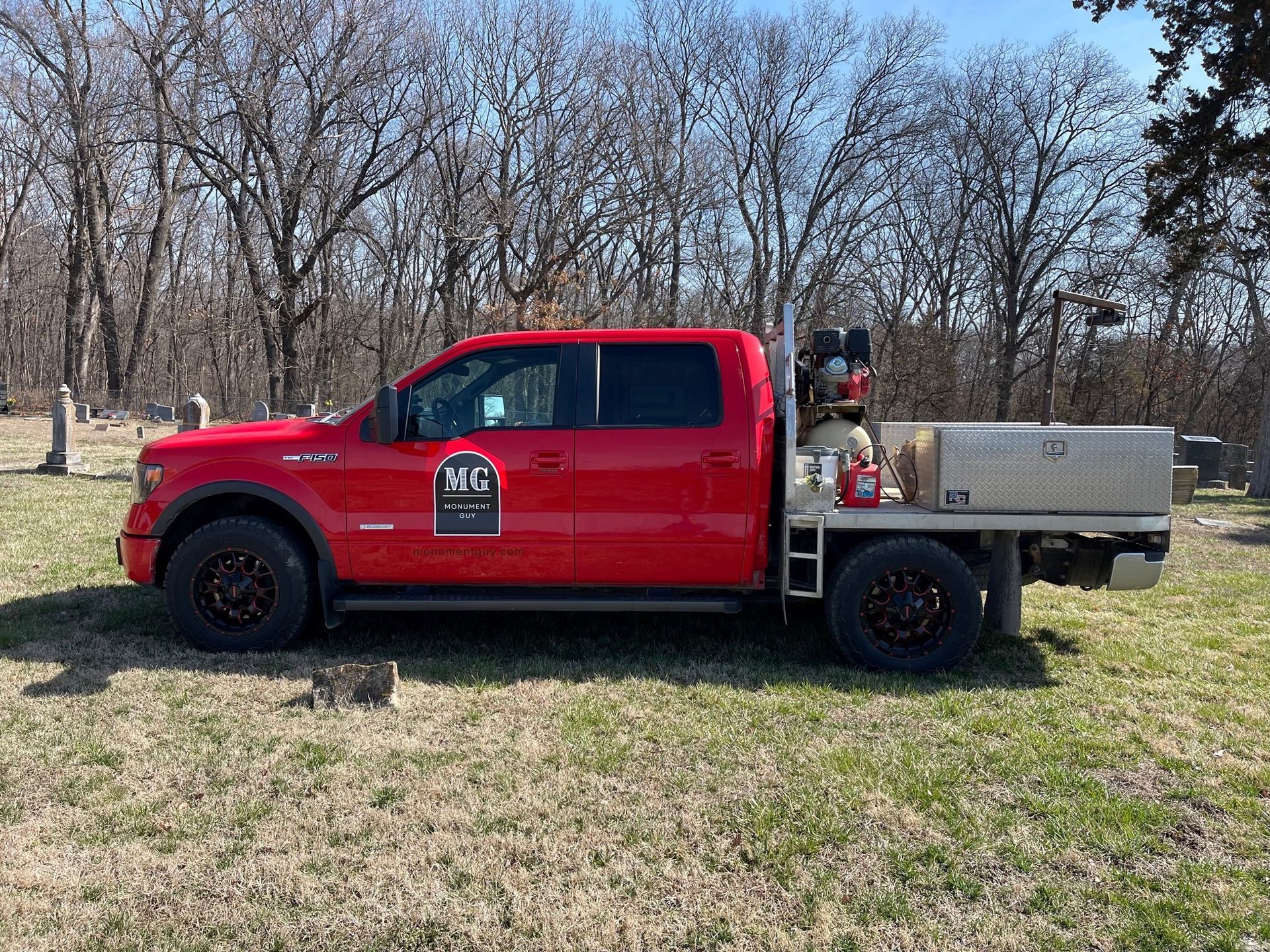a red truck is parked in a grassy field with trees in the background .