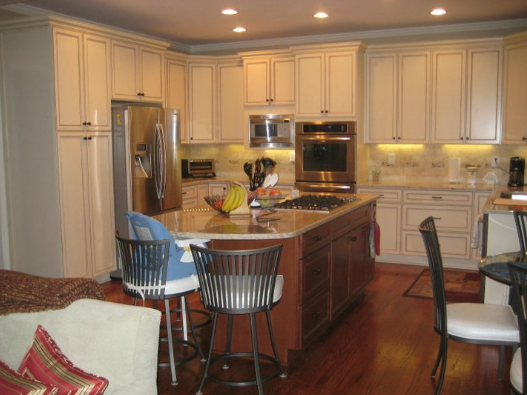 Cream-colored kitchen with stainless steel appliances, wooden island, and dark wood floors. Includes seating at the island.