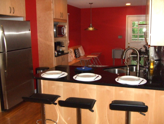Kitchen with stainless steel refrigerator, black countertops, red wall, and breakfast bar with three stools.
