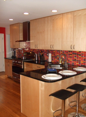 Modern kitchen with light wood cabinets, black countertops, colorful backsplash, and island with stools.