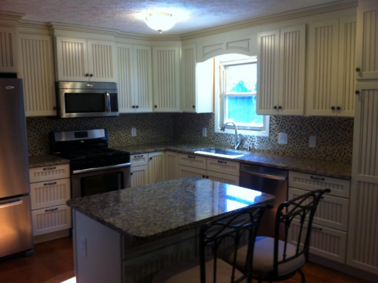 Kitchen with cream cabinets, granite countertops, and an island with a barstool.
