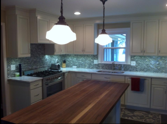Kitchen with white cabinets, tile backsplash, brown island, and pendant lights.