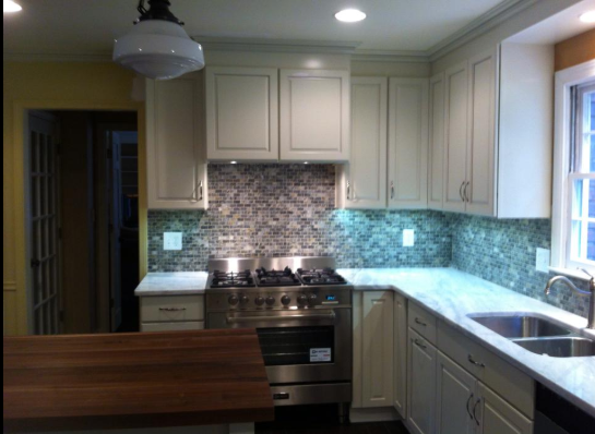 Cream kitchen with stainless steel stove, mosaic backsplash, butcher block island, and window.