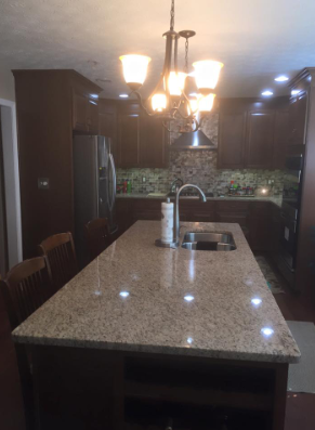 Kitchen with a large island, granite countertop, dark wood cabinets, and pendant lighting.