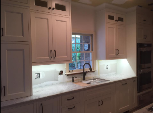 White kitchen cabinets with a sink, window, and under-cabinet lighting.