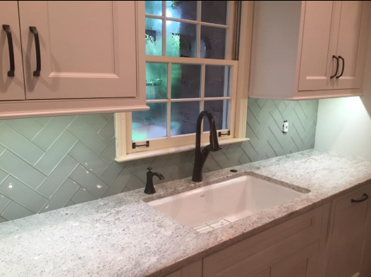 Kitchen sink with white cabinets, light blue backsplash, and a dark faucet and hardware.
