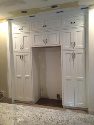 White kitchen cabinets surrounding a refrigerator space, with a granite countertop in front.