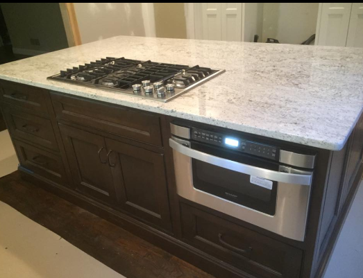 Kitchen island with a gas stovetop, built-in microwave, and granite countertop; brown cabinetry.