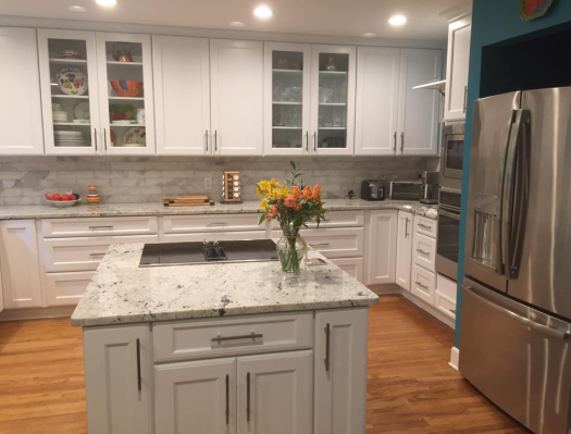 White kitchen with granite countertops, island with cooktop, stainless steel refrigerator.