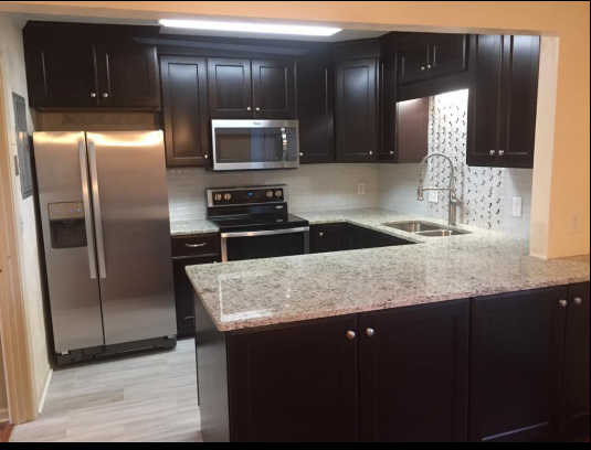 Dark brown kitchen with stainless steel appliances, light countertops, and white tile backsplash.