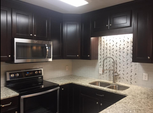 Dark brown kitchen cabinets, stainless steel appliances, and a patterned backsplash.