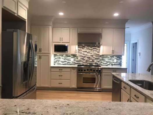 A bright kitchen with white cabinets, stainless steel appliances, and a colorful backsplash.
