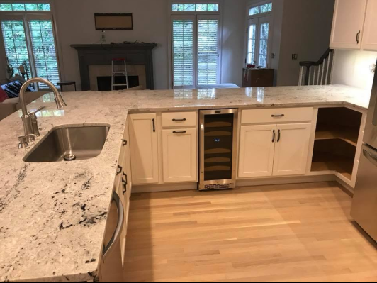 White kitchen island with granite countertop, cabinets, and wine cooler. Light wood floor.