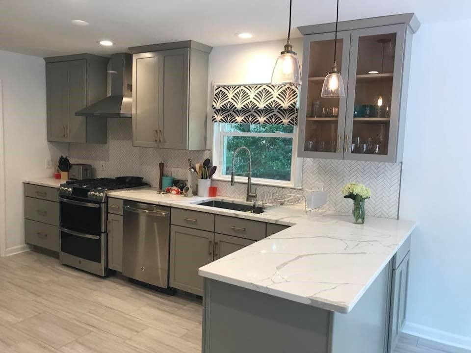 Modern kitchen with gray cabinets, white countertops, stainless steel appliances, and a window with a patterned shade.
