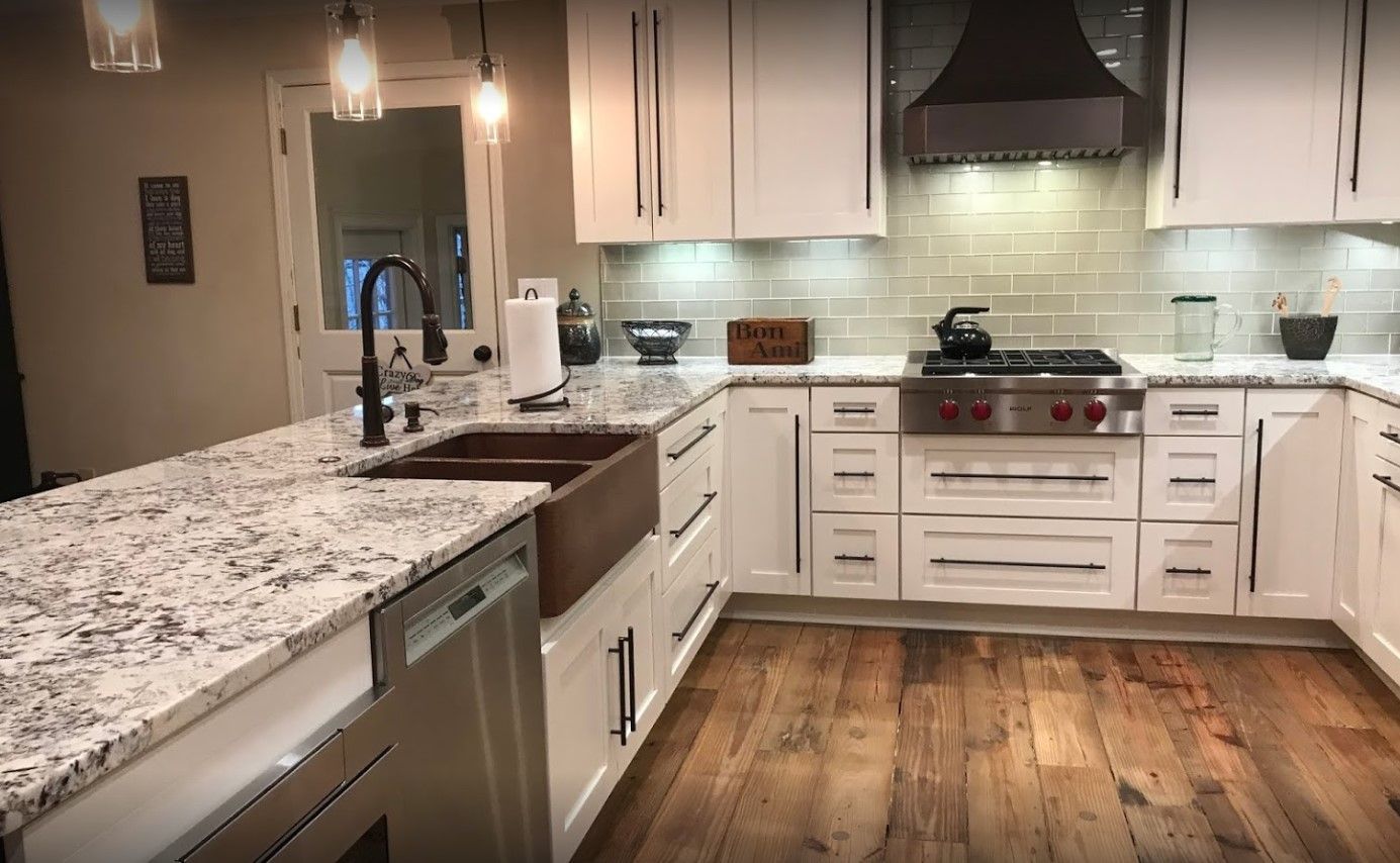 White kitchen with granite countertops, stainless steel appliances, wooden floors.