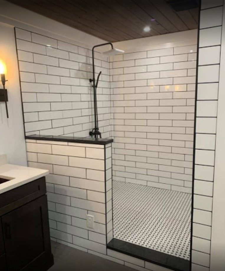 Bathroom with white subway tile shower, black trim, and dark fixtures. Black and white tile floor.