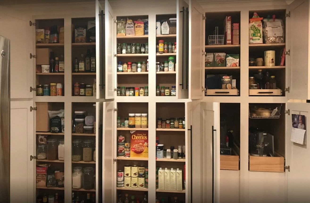 Kitchen pantry with open white cabinets, filled with organized food items, jars, and spices.