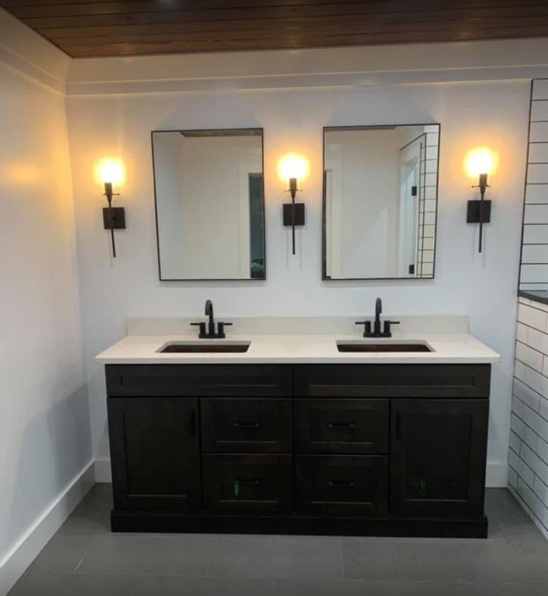 A bathroom with a dark brown vanity, two mirrors, and sconce lighting.