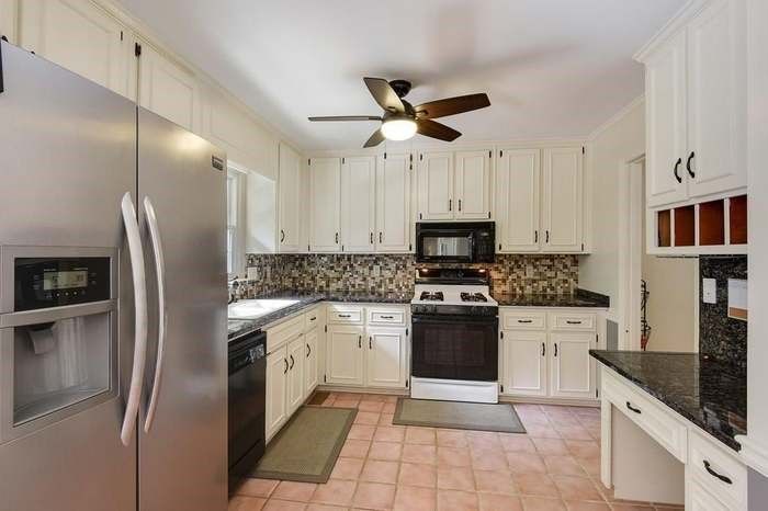 Kitchen with white cabinets, stainless steel fridge, black appliances, and pink tile floor.