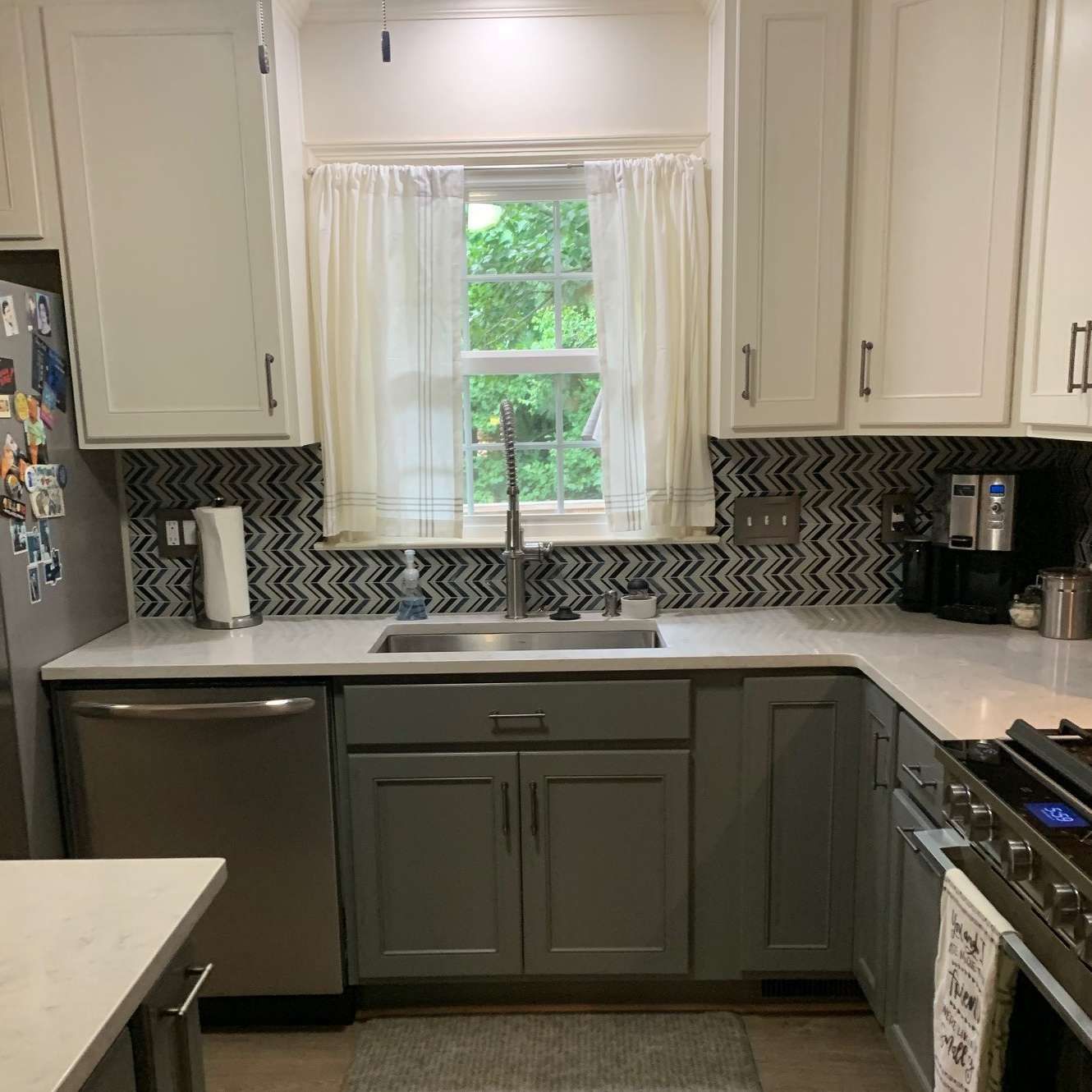 Kitchen with white and gray cabinets, patterned backsplash, window above sink, and stainless steel appliances.