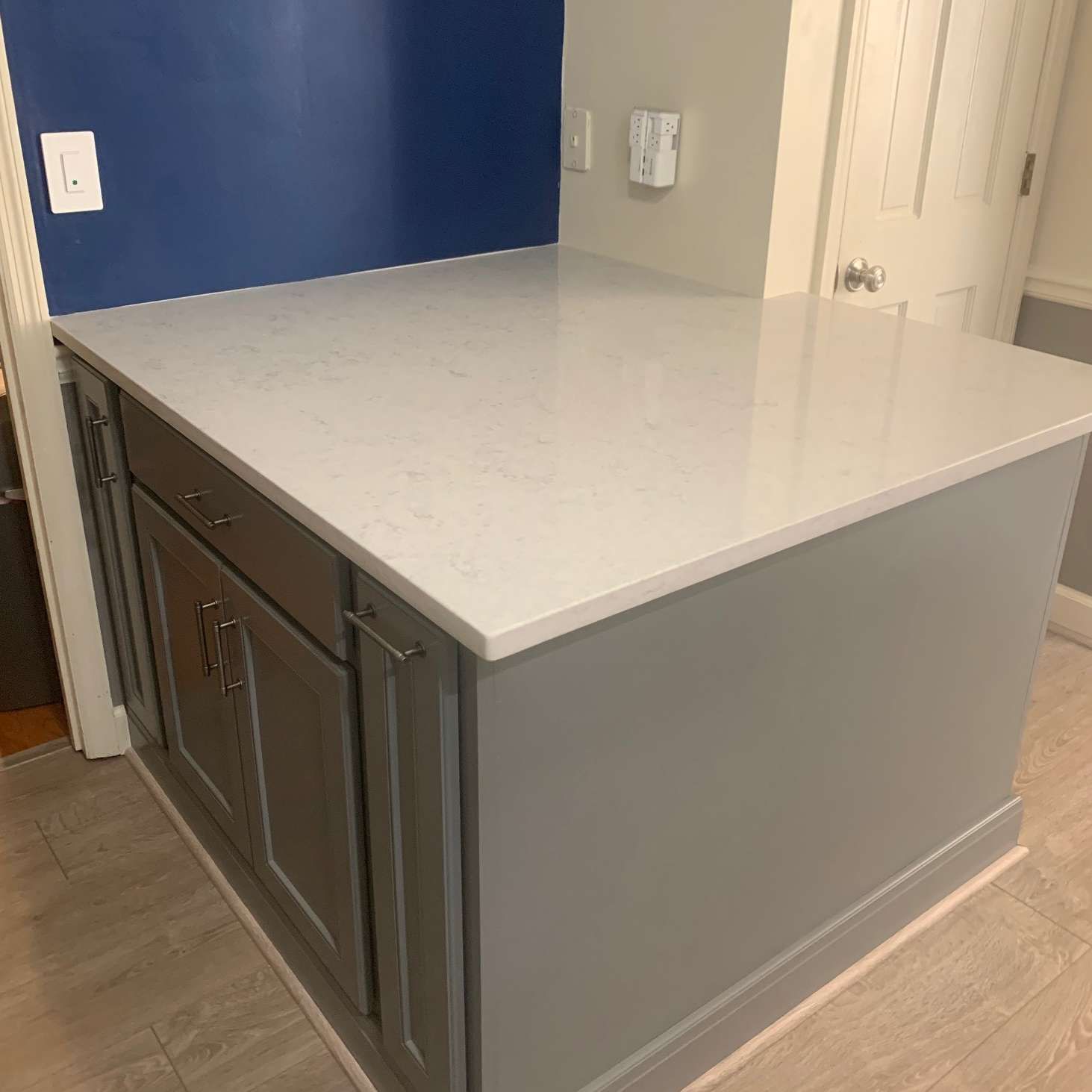 Gray kitchen island with white countertop, gray cabinets, and blue wall.