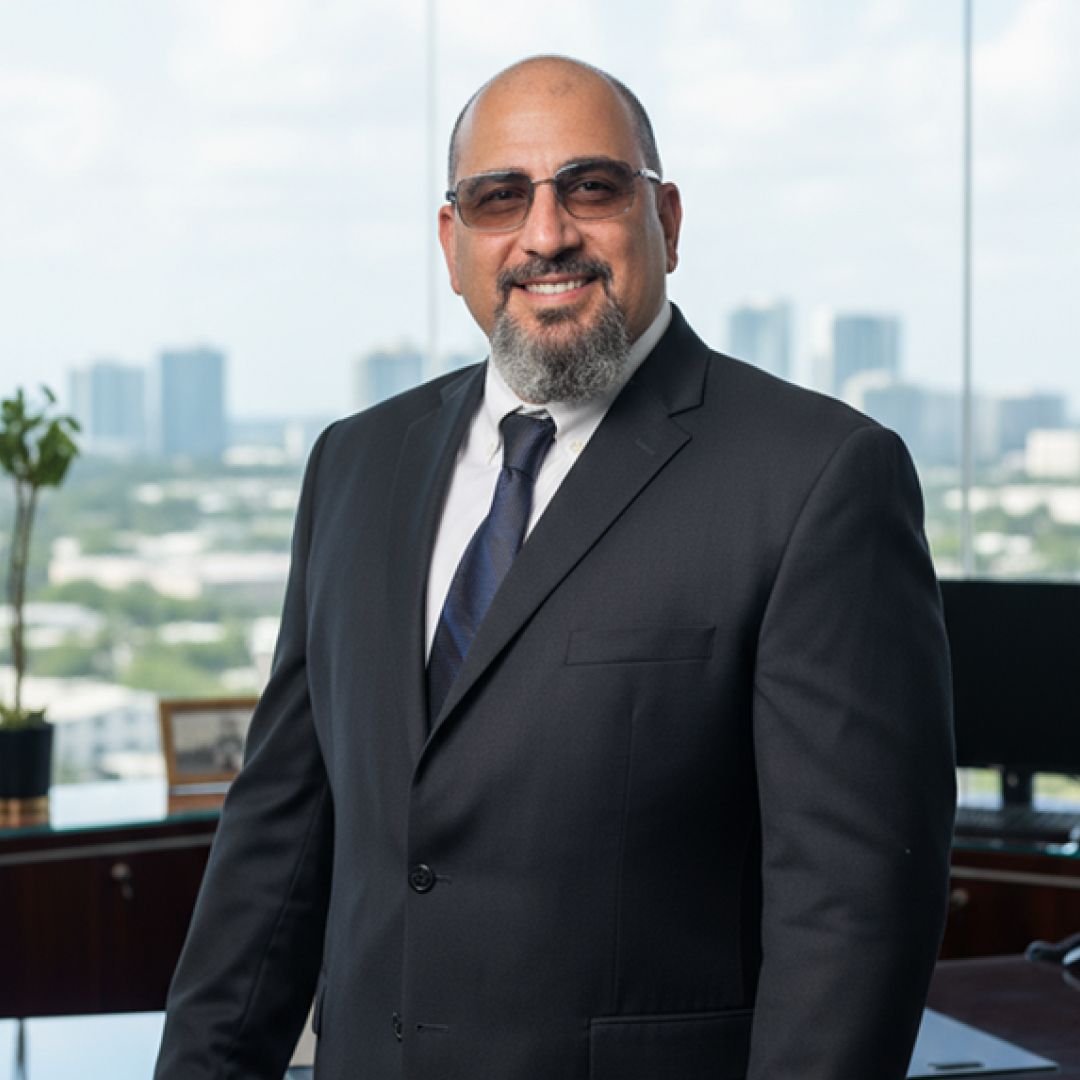 Man in a suit smiles, standing near a window with city skyline in the background.