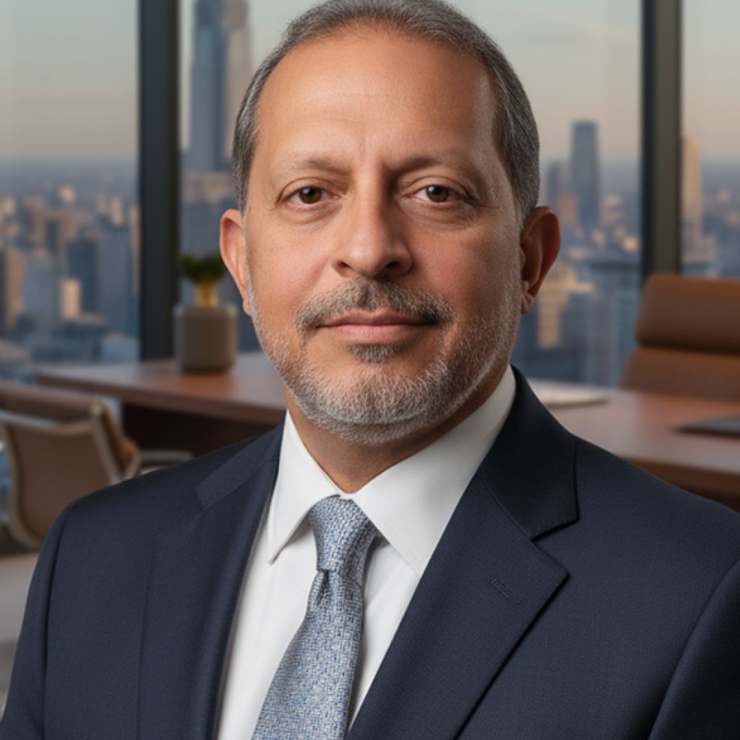 Man in a suit and tie, looking at the viewer; office setting with city view.