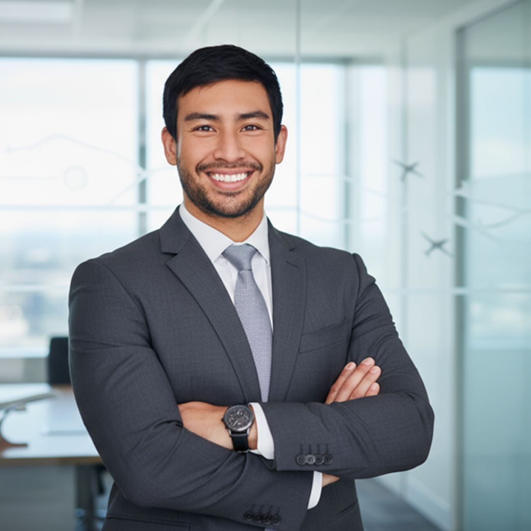 Man in suit with arms crossed, smiling in an office setting.