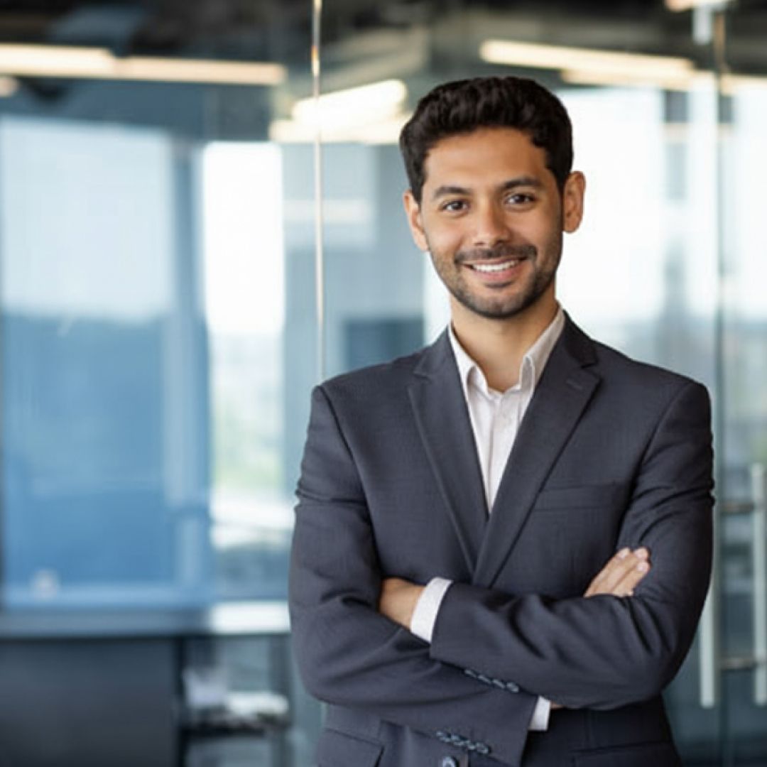 Man in suit, arms crossed, smiling in an office setting with glass walls.