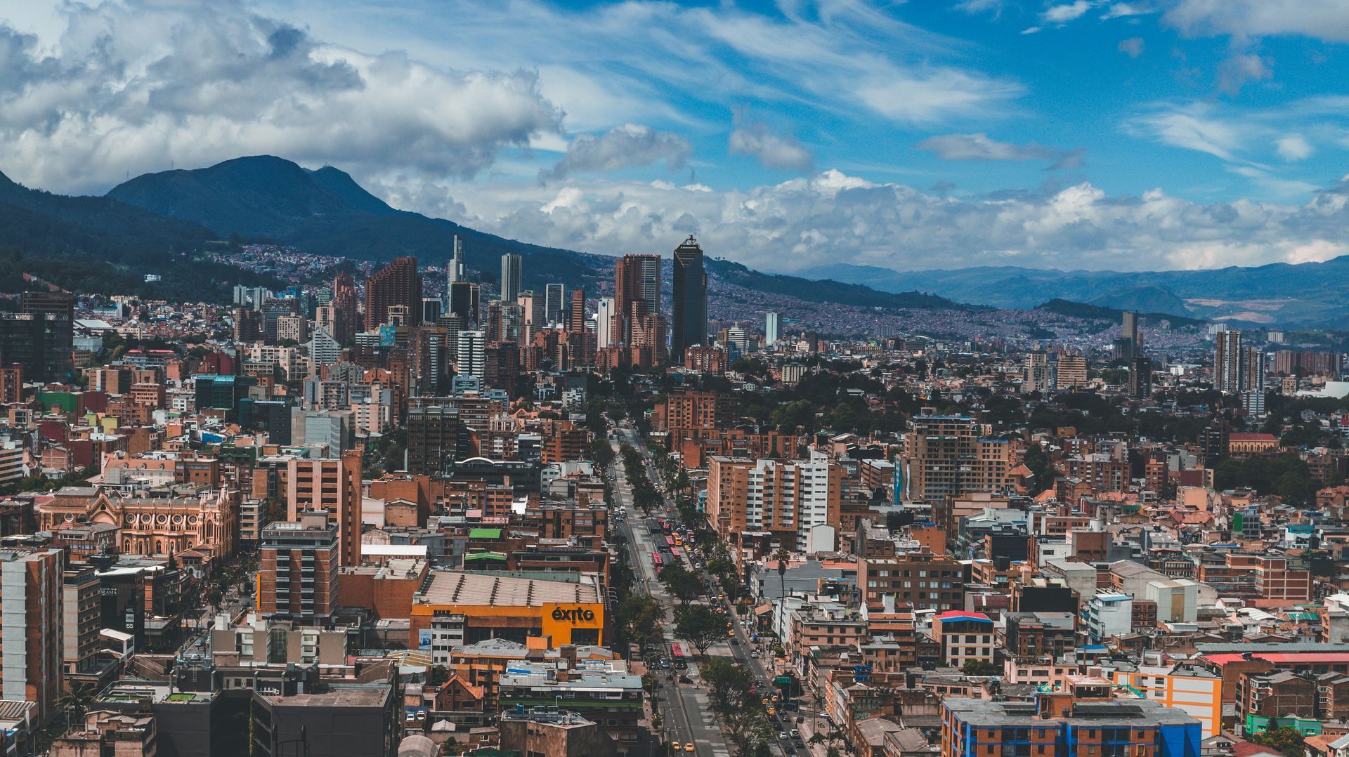 Cityscape of Bogotá, Colombia, with tall buildings, a long road, and mountains in the distance under a blue sky.