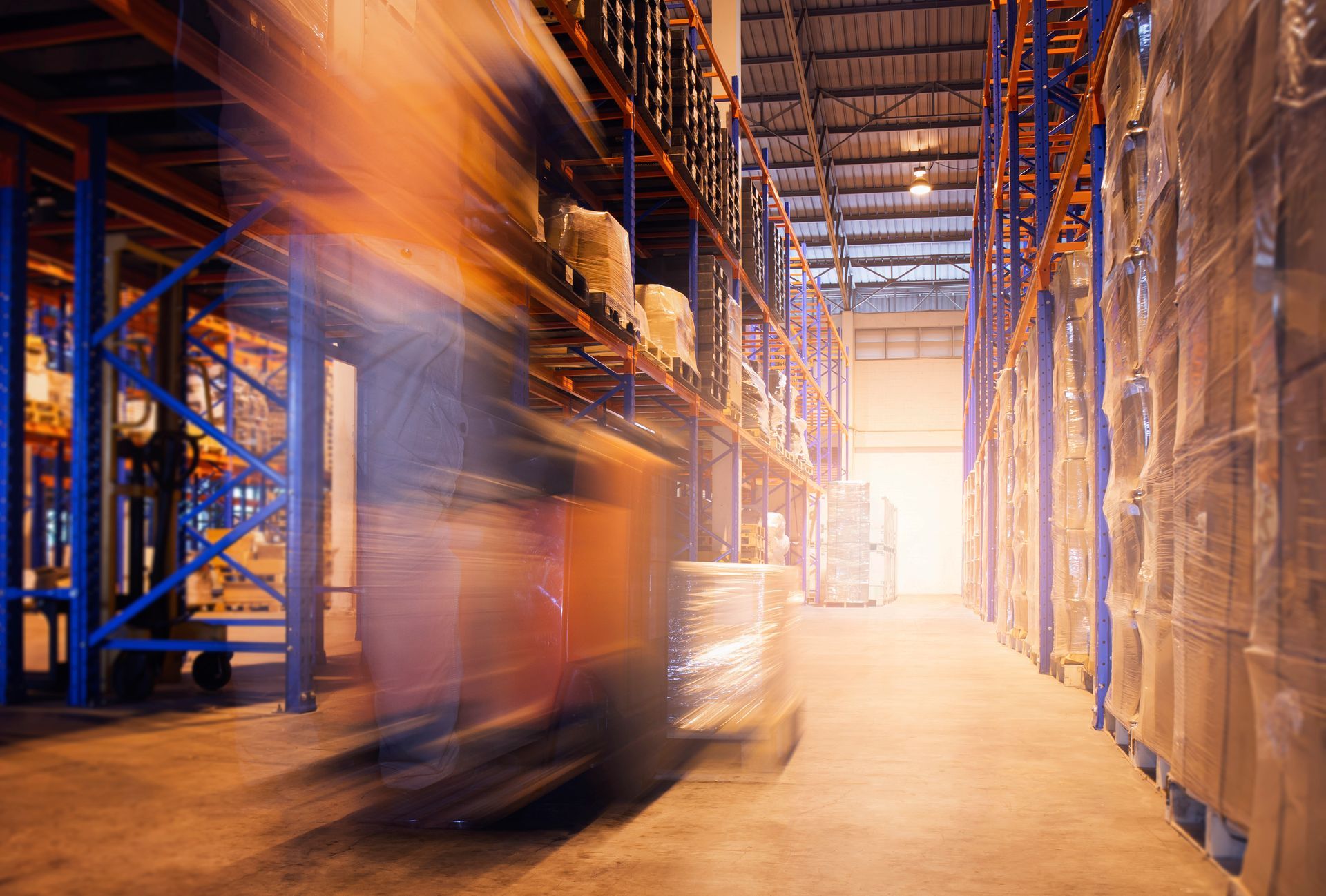 Blurred warehouse scene with a forklift moving goods along shelving.