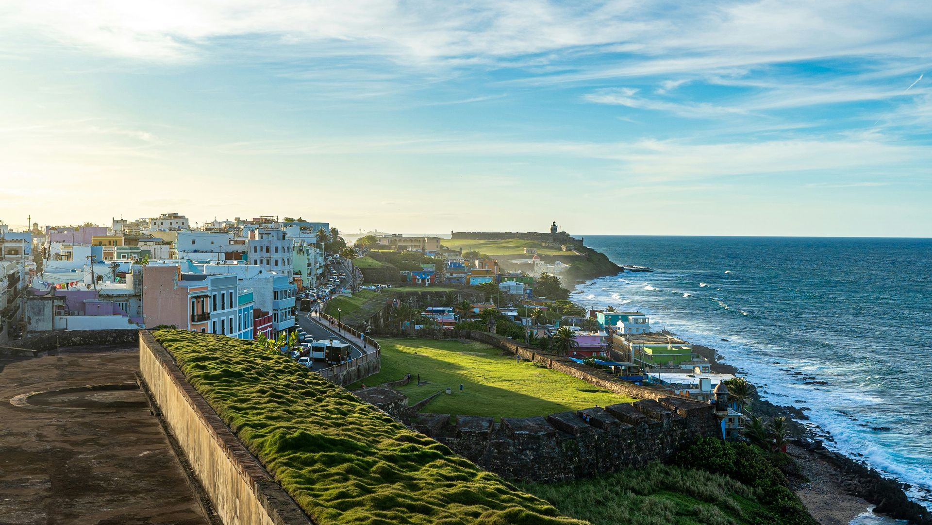 Coastal view of San Juan, Puerto Rico. Historic buildings line the shore next to the ocean under a blue sky.