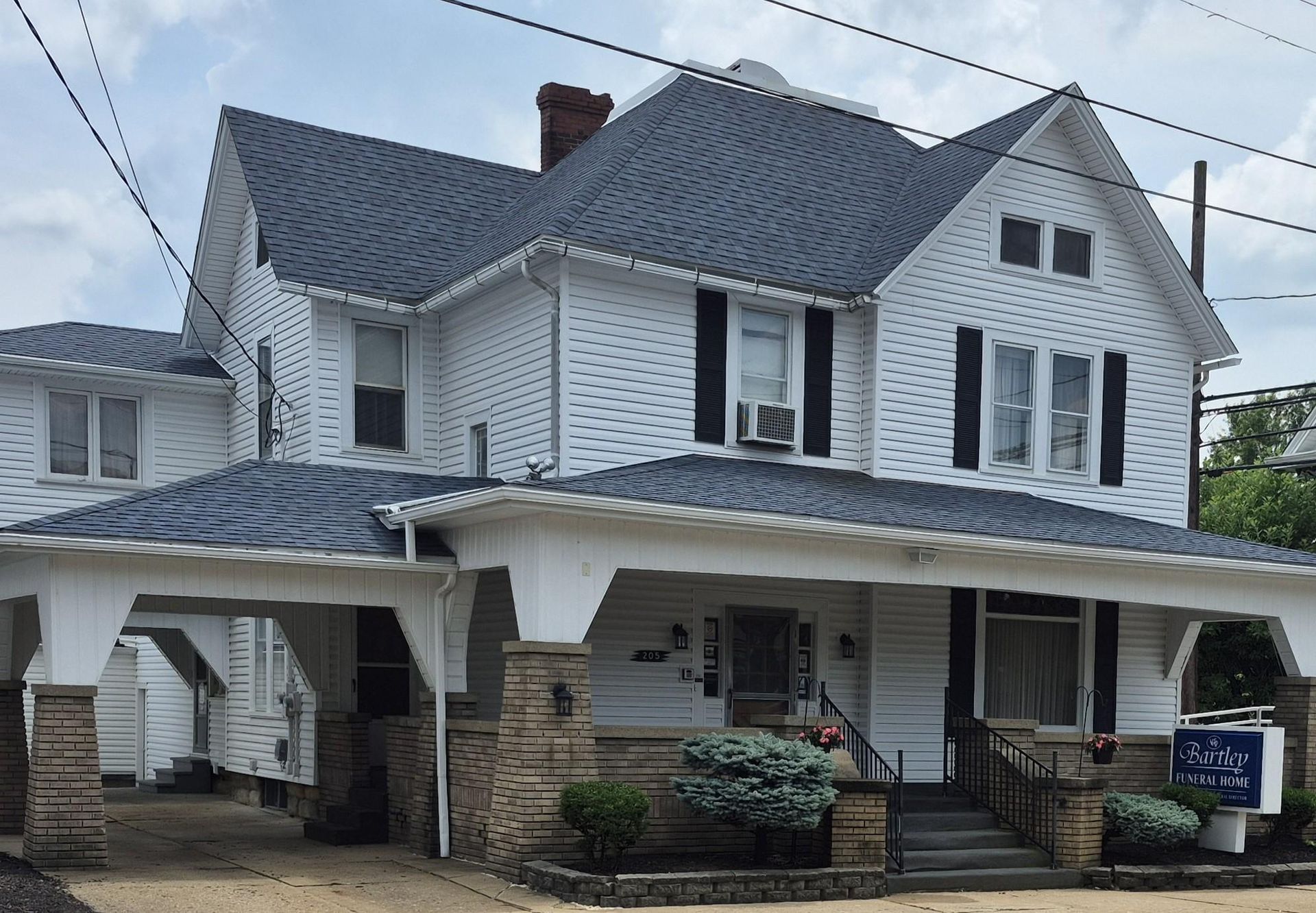 White two-story house with dark blue roof, porch, carport, and black shutters.